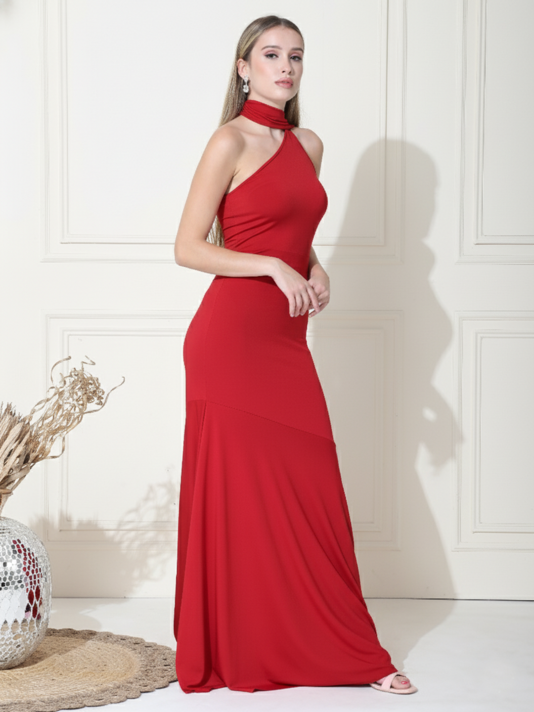 Woman wearing a red halter neck gown against a white wall.